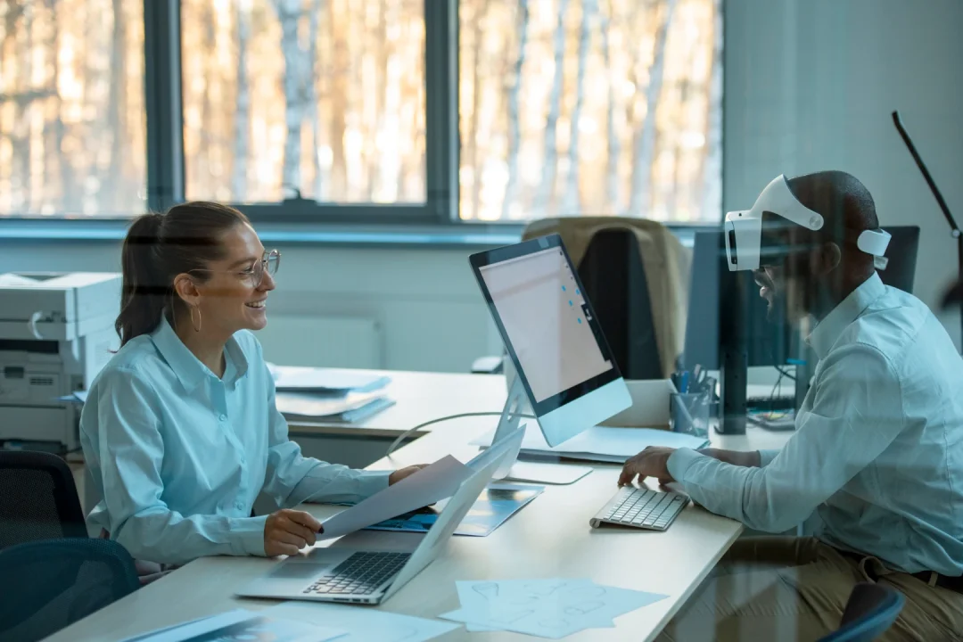 Two professionals discussing work while using AI-powered technology in a modern office environment.